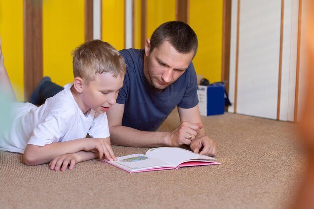 Lindo filho lê um livro para o pai deitado no chão