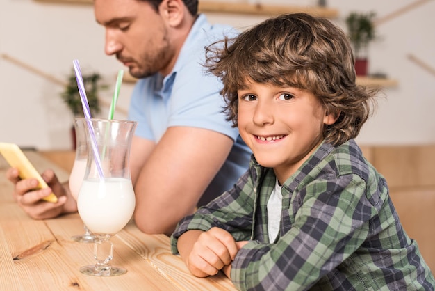 Lindo filho sorridente e seu pai bebendo milk-shakes no café