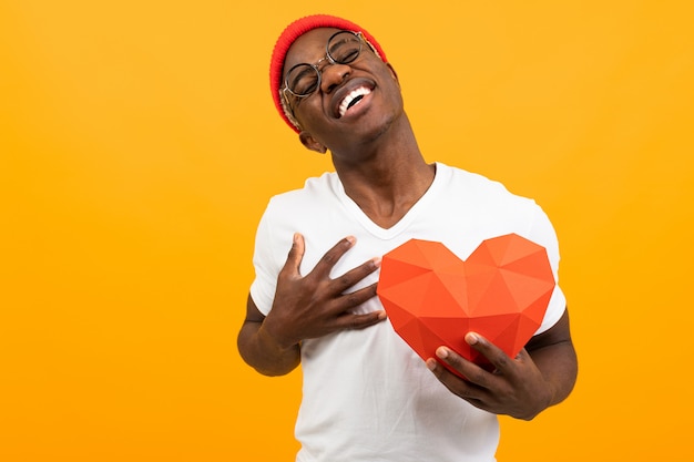 Lindo guapo americano en camiseta blanca tiene corazón 3d hecho de papel para el día de San Valentín en amarillo con espacio de copia