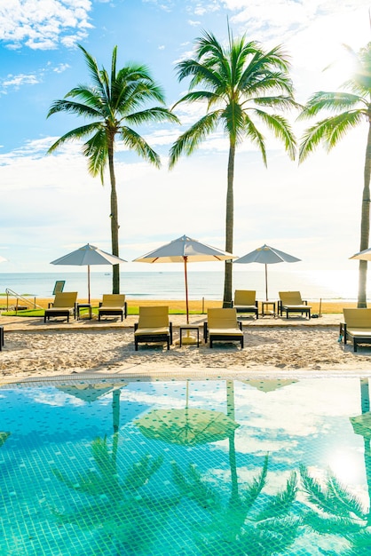 Foto lindo guarda-chuva de luxo e cadeira ao redor da piscina ao ar livre no hotel e resort com coqueiro em férias de céu azul e conceito de férias