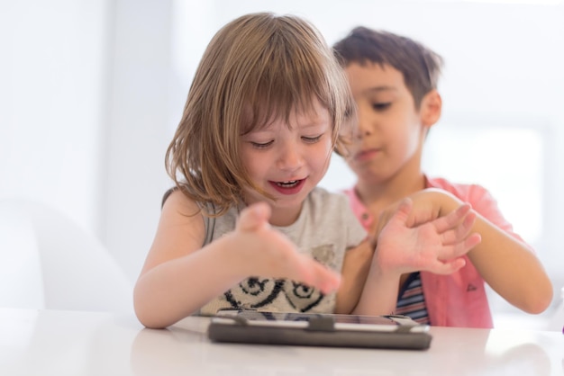 lindo hermanito y hermana divirtiéndose en casa los niños jugando en la computadora de la tableta