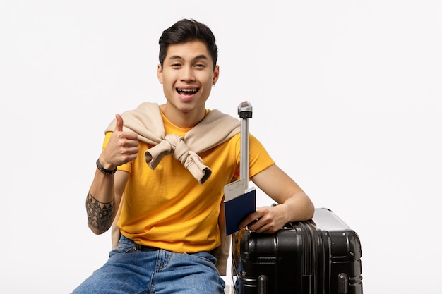 Lindo hombre asiático en camiseta amarilla lista para viajar con pasaporte y bolsa de carro