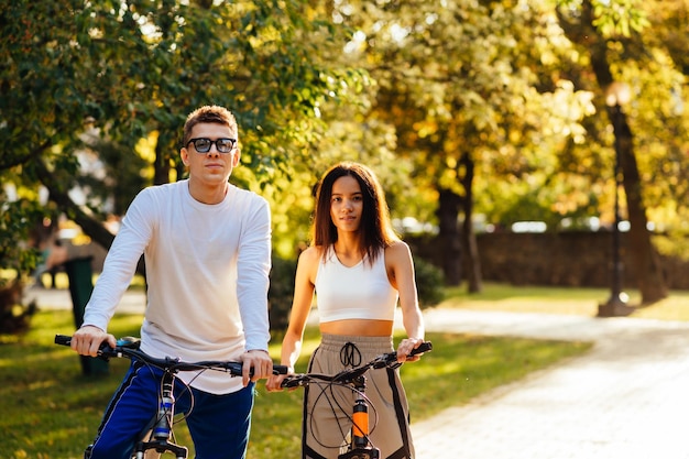 Lindo homem e mulher em roupas casuais elegantes ficam no parque outono em bicicletas