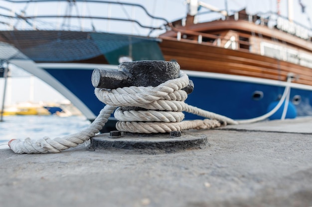 lindo iate caro é amarrado com uma corda a um poste de metal no porto. navio do mar está parado em uma doca. Close do cabo e âncora de metal. Conceito de seguro. Viajar no mar