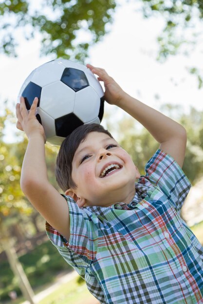 Lindo joven jugando con una pelota de fútbol al aire libre en el parque