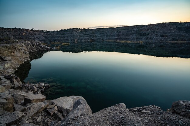Lindo lago cercado por grandes pilhas de resíduos de pedra do trabalho árduo em uma mina contra um lindo céu noturno com estrelas