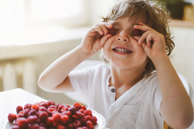 Lindo lindo garotinho comendo framboesas frescas. Alimentação saudável, infância e desenvolvimento.
