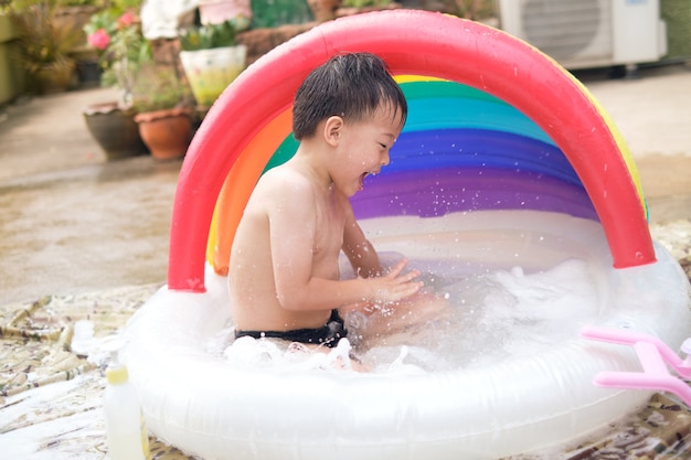 Lindo menino asiático de 5 anos se divertindo na piscina inflável brincando sozinho em casa