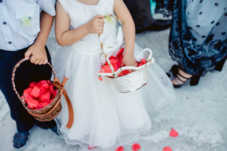 Foto lindo menino e uma menina em um vestido branco e terno com cesta jogando pétalas de rosas vermelhas no casamento