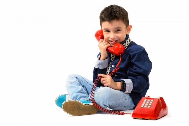 lindo menino feliz sorrindo e falando no telefone antigo