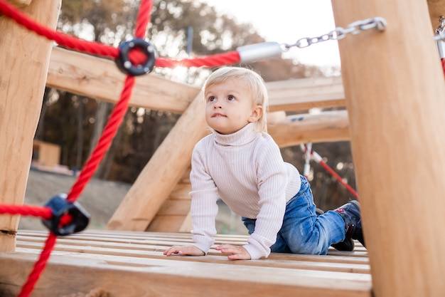 Lindo menino loiro brincando em um playground esportivo de madeira ao ar livre