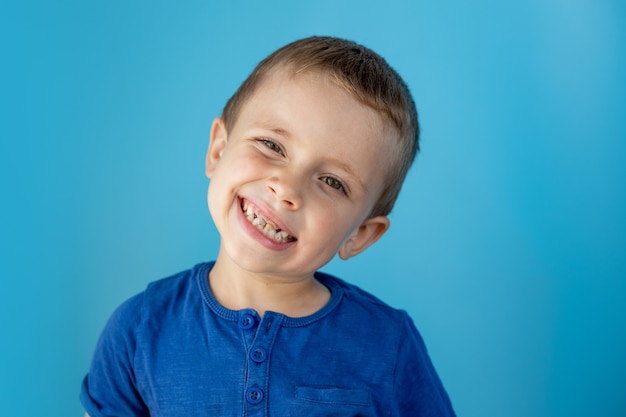 Lindo menino mostra a língua e se diverte com o fundo da parede azul.