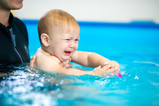 lindo menino triste aprendendo a nadar em uma piscina especial para crianças pequenas