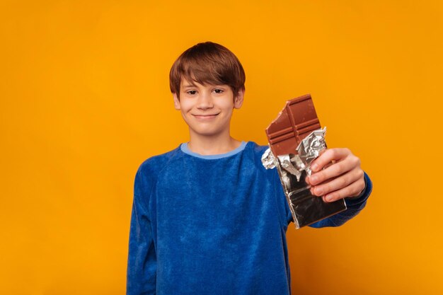 Foto lindo muchacho adolescente sonriente está mostrando una barra de chocolate mordida a la cámara