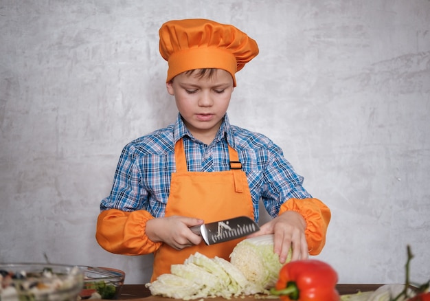 Foto lindo muchacho europeo corta el repollo chino con un cuchillo en la tabla de cortar para ensalada de verduras