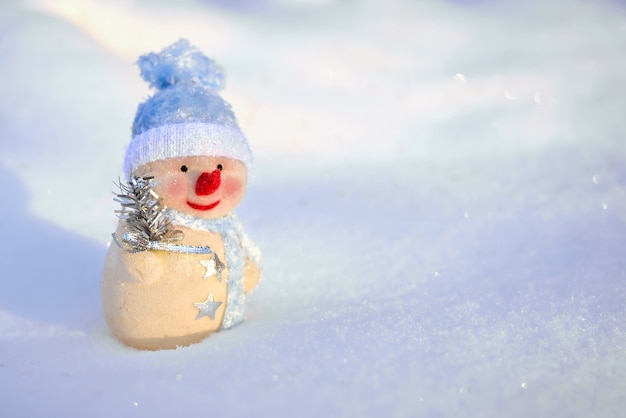 Un lindo muñeco de nieve de juguete con una gorra azul en la nieve en invierno