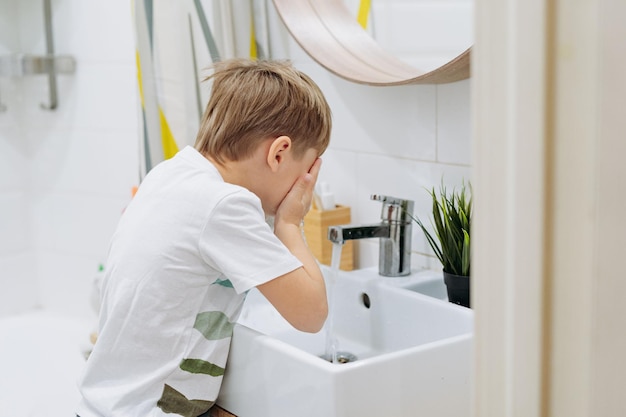 Lindo niño de 6 años lavándose la cara sobre el lavabo en el baño Imagen con enfoque selectivo