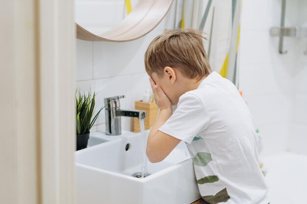 Lindo niño de 6 años lavándose la cara sobre el lavabo en el baño Imagen con enfoque selectivo