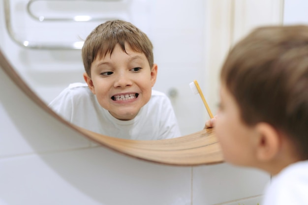 Lindo niño de 8 años lavándose la cara en el baño mirándose en el espejo y sonriendo