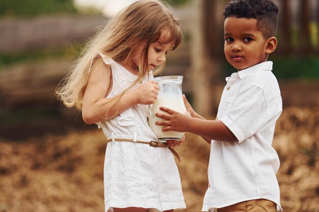 Lindo niño afroamericano con niña europea está en la granja con leche