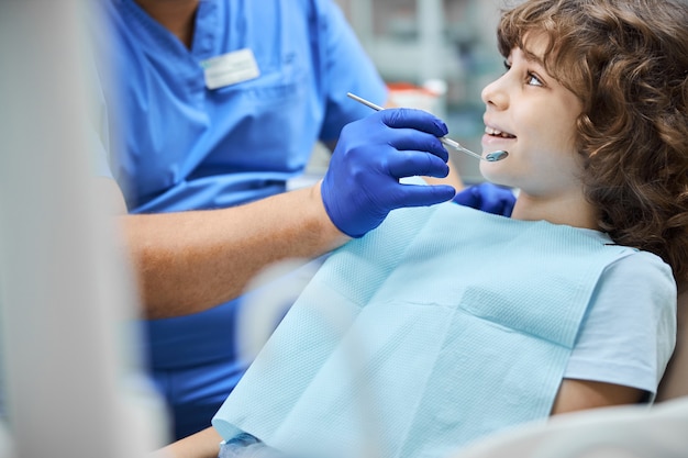 Lindo niño alegre sonriendo mientras el dentista sostiene un espejo dental cierra la boca