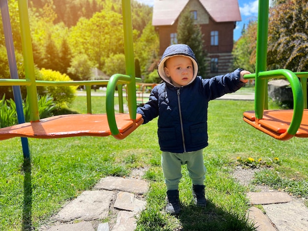 Un lindo niño de un año y medio parado cerca del columpio Patio trasero de la casa Entretenimiento infantil Enfoque selectivo