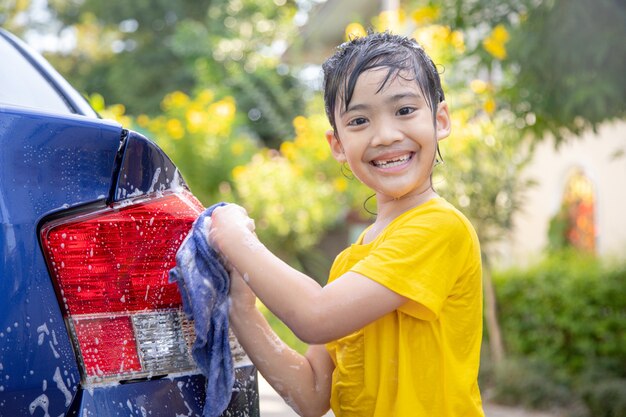 Lindo niño asiático lavando un coche con manguera en verano
