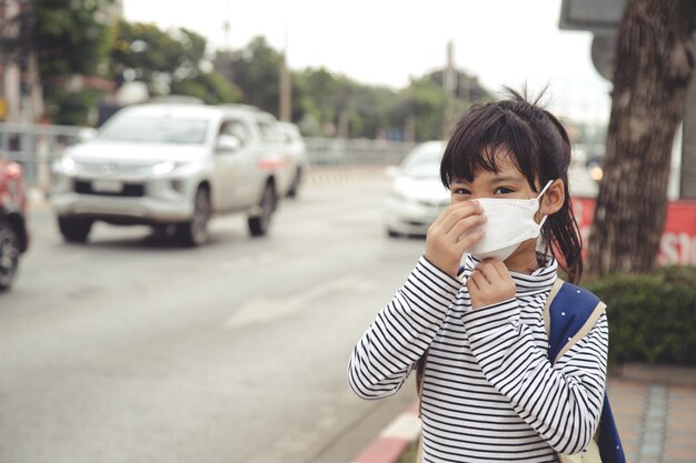 Lindo niño asiático niña con máscara de protección contra la contaminación atmosférica por smog con PM 2.5 en la ciudad