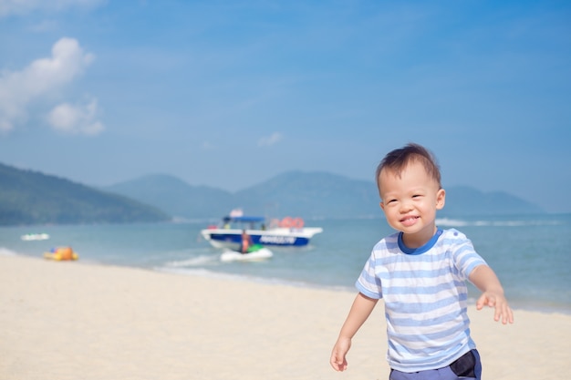 Lindo niño asiático niño corriendo en la playa tropical de arena en las vacaciones de verano, los niños juegan en el mar