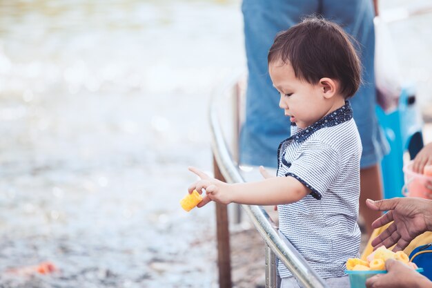 Lindo niño asiático niño divirtiéndose para alimentar y dar comida a los peces en el estanque