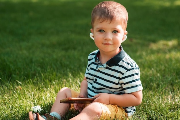 Un lindo niño de aspecto europeo sostiene un teléfono inteligente en la mano en primer plano con auriculares inalámbricos