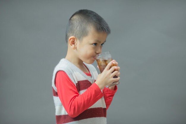 Lindo niño bebiendo agua de vidrioPequeño niño asiático bebiendo refresco