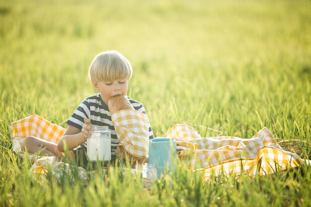 Lindo niño bebiendo leche al aire libre. Chico alegre en el picnic