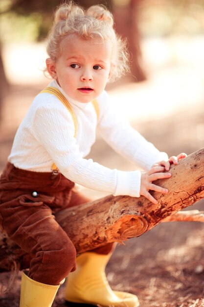 Divertida y linda niña de 4 a 5 años que usa gafas de sol y un vestido de  punto amarillo posando sobre la naturaleza en otoño