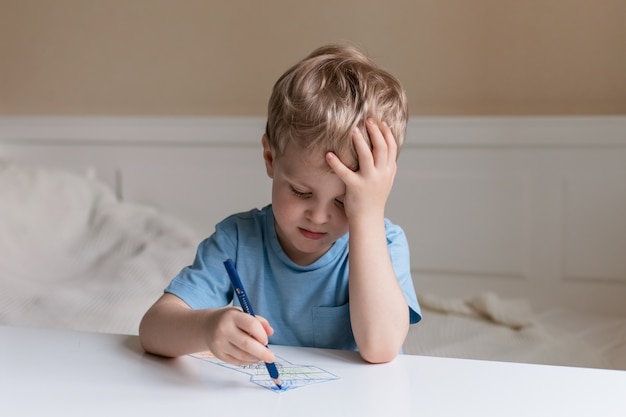 Lindo niño con cabello rubio sentado en una mesa