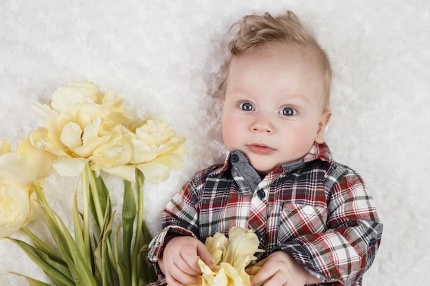 Lindo niño en una camisa a cuadros tiene un ramo de tulipanes amarillos