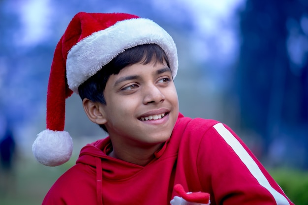 Un lindo niño con camiseta roja de gorro de Papá Noel, sonriendo felizmente durante la época navideña