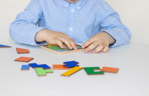 lindo niño de cara seria en una mesa blanca jugando con un rompecabezas de tangram de siete polígonos planos