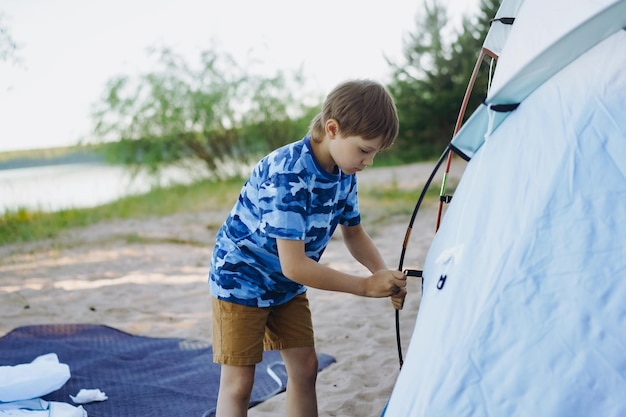 Lindo niño caucásico ayudando a montar una tienda de campaña Concepto de camping familiar