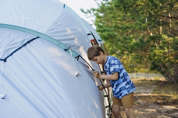 Lindo niño caucásico ayudando a montar una tienda de campaña Concepto de camping familiar