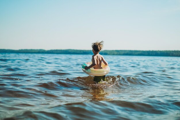 Lindo niño caucásico corriendo hacia el agua con salpicaduras y risas Vacaciones en el mar Infancia feliz Imagen con enfoque selectivo