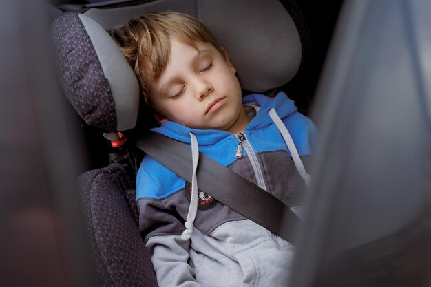 Lindo niño caucásico durmiendo en un asiento para niños abrochado con cinturón vacaciones familiares por concepto de automóvil