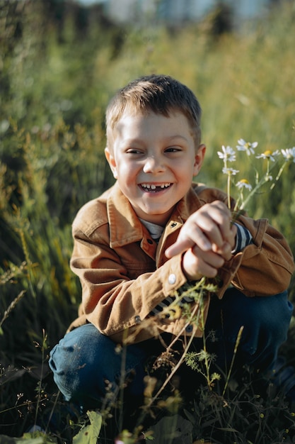 Foto lindo niño caucásico sonriendo sentado en el claro sosteniendo un ramo de flores