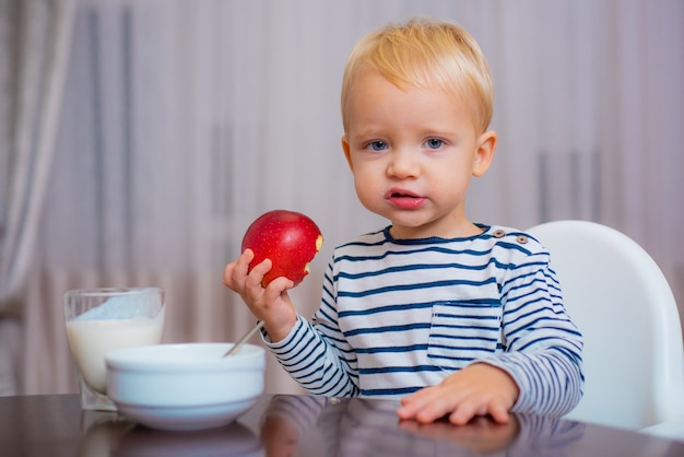 Lindo niño comiendo su comida, sosteniendo una manzana en su mano, sonriendo.