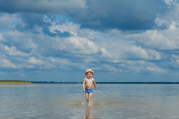 Lindo niño corriendo por el agua en la playa