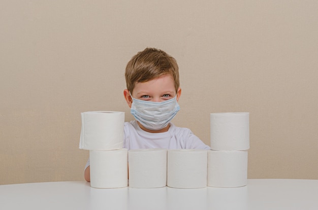 Lindo niño de cuatro años con una máscara médica protectora juega con papel higiénico: construye una pared protectora. Cuarentena domiciliaria con niños, ocio familiar.