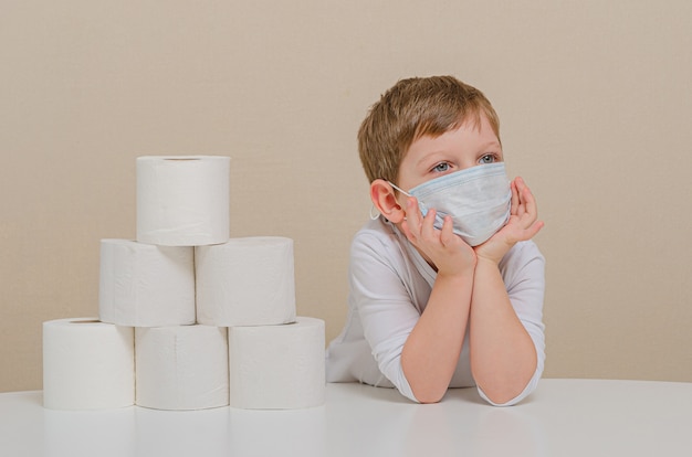 Lindo niño de cuatro años en una máscara médica protectora juega con papel higiénico