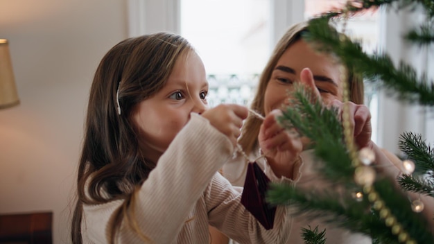 Lindo niño decorando el árbol de Navidad con mamá casa primer plano madre abrazando hija