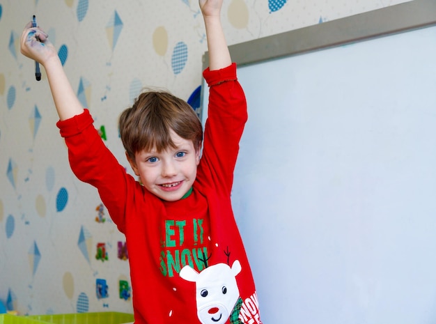 Lindo niño dibujando en una pizarra blanca con rotulador y sonriendo Concepto de educación temprana