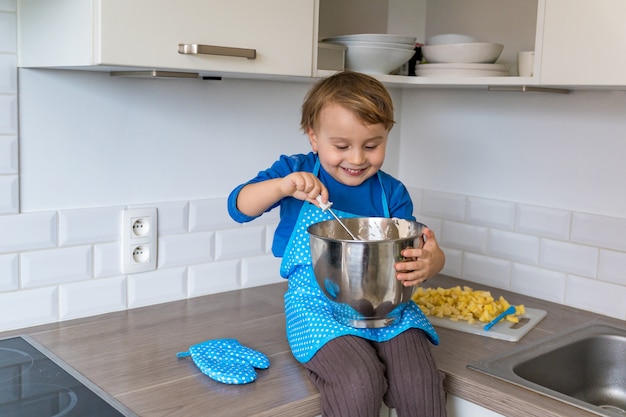 Lindo niño divertido hornear tarta de manzana en la cocina doméstica